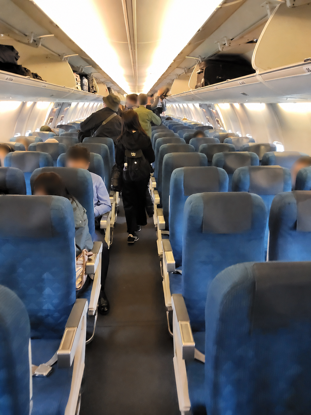 ジンエアー機内に並ぶ青い座席と荷物を収納する乗客